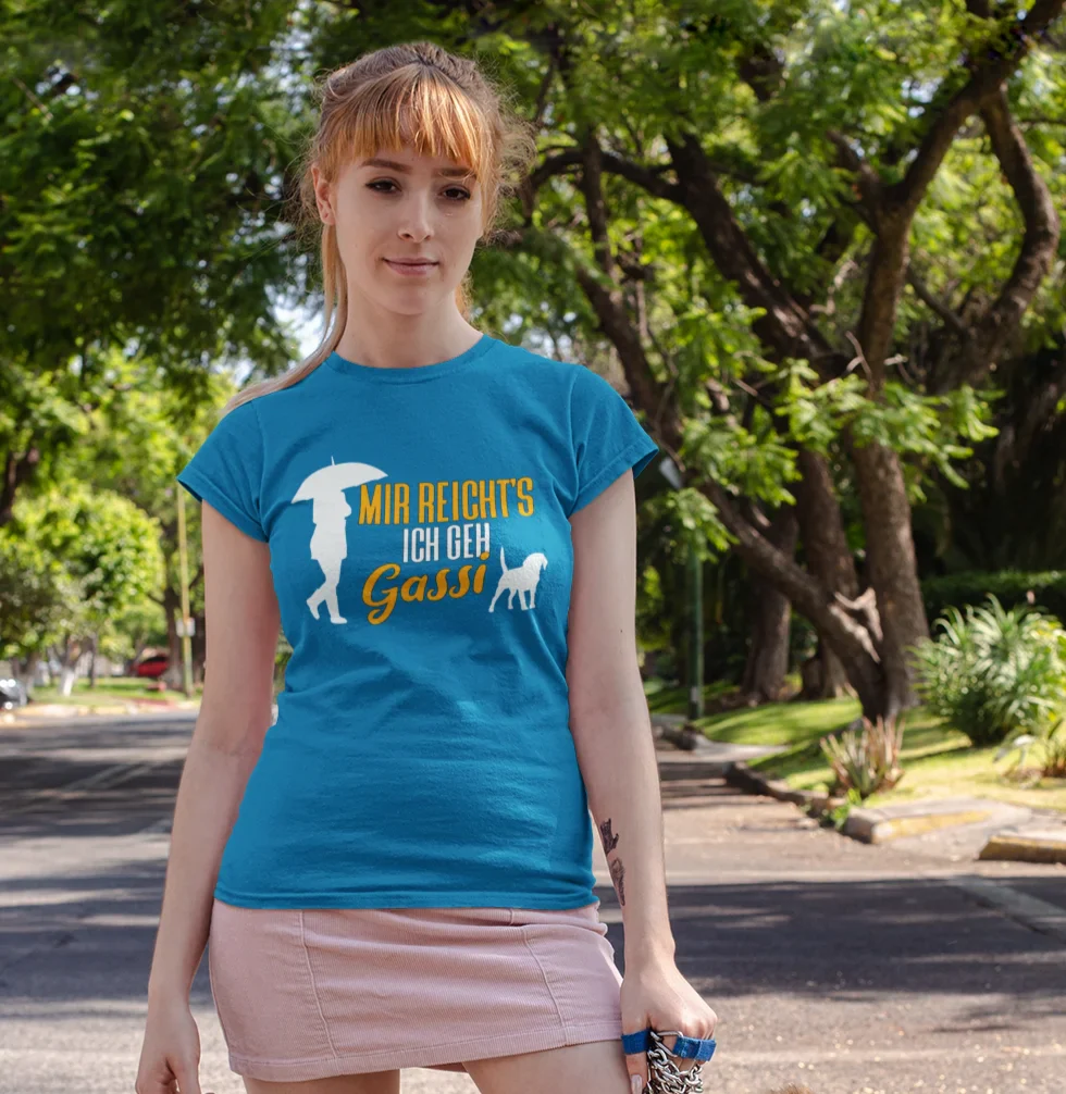 Frau im blauen T-Shirt mit Aufdruck ‚Mir reicht’s – ich geh Gassi‘ steht mit einem Collie auf einer sonnigen Straße – witziges Hundemotiv für Hundeliebhaberinnen.