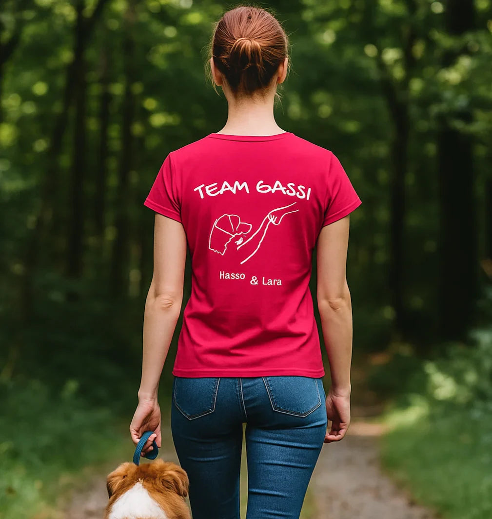 Frau mit rotem personalisiertem ‘Team Gassi’-T-Shirt und Hund auf Waldweg - Rückansicht, personalisiertes Hundemotiv auf dem Rücken, Szene in natürlicher Umgebung